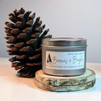 Candle in a metal tin with a pine cone on a wooden coaster against a light background