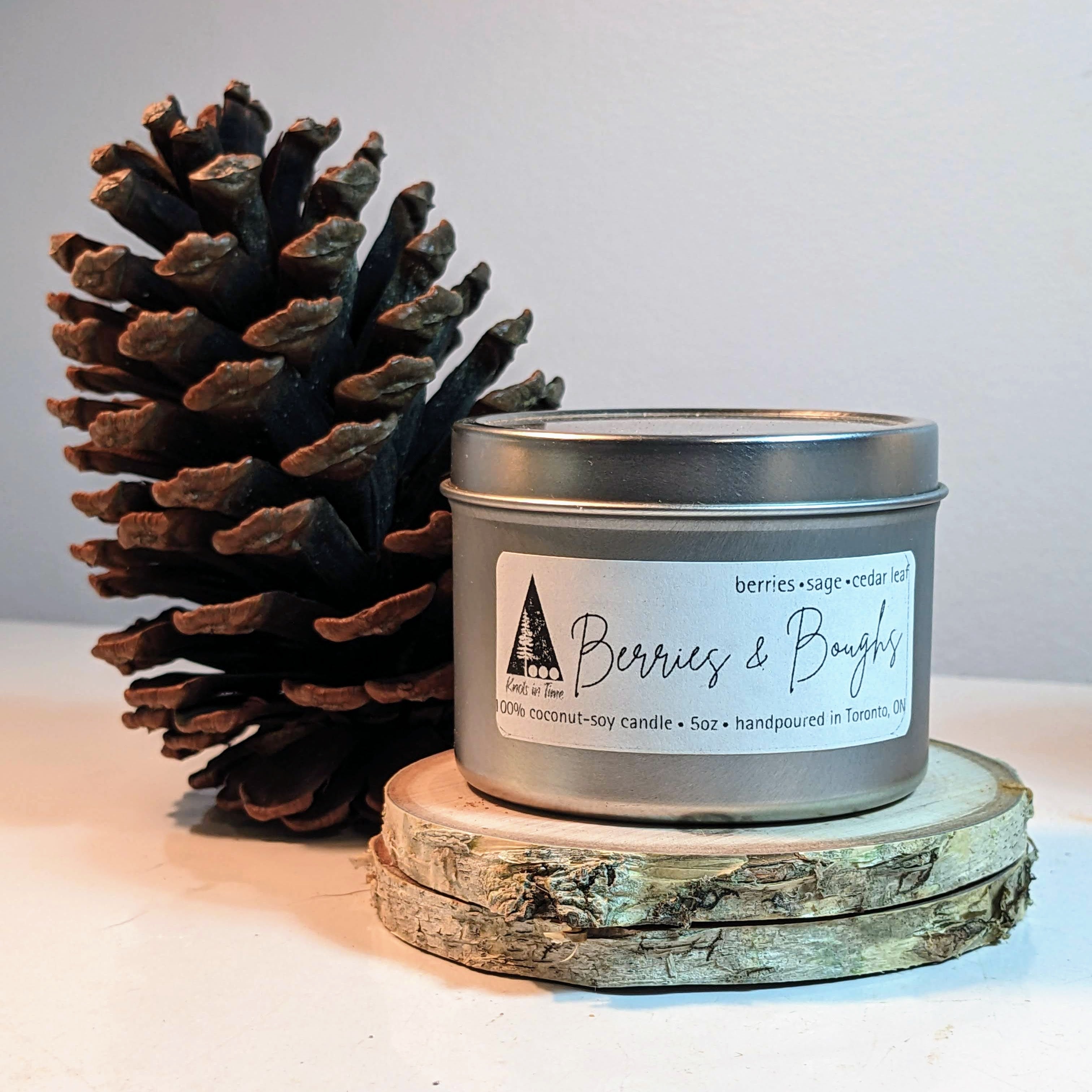 Candle in a metal tin with a pine cone on a wooden coaster against a light background