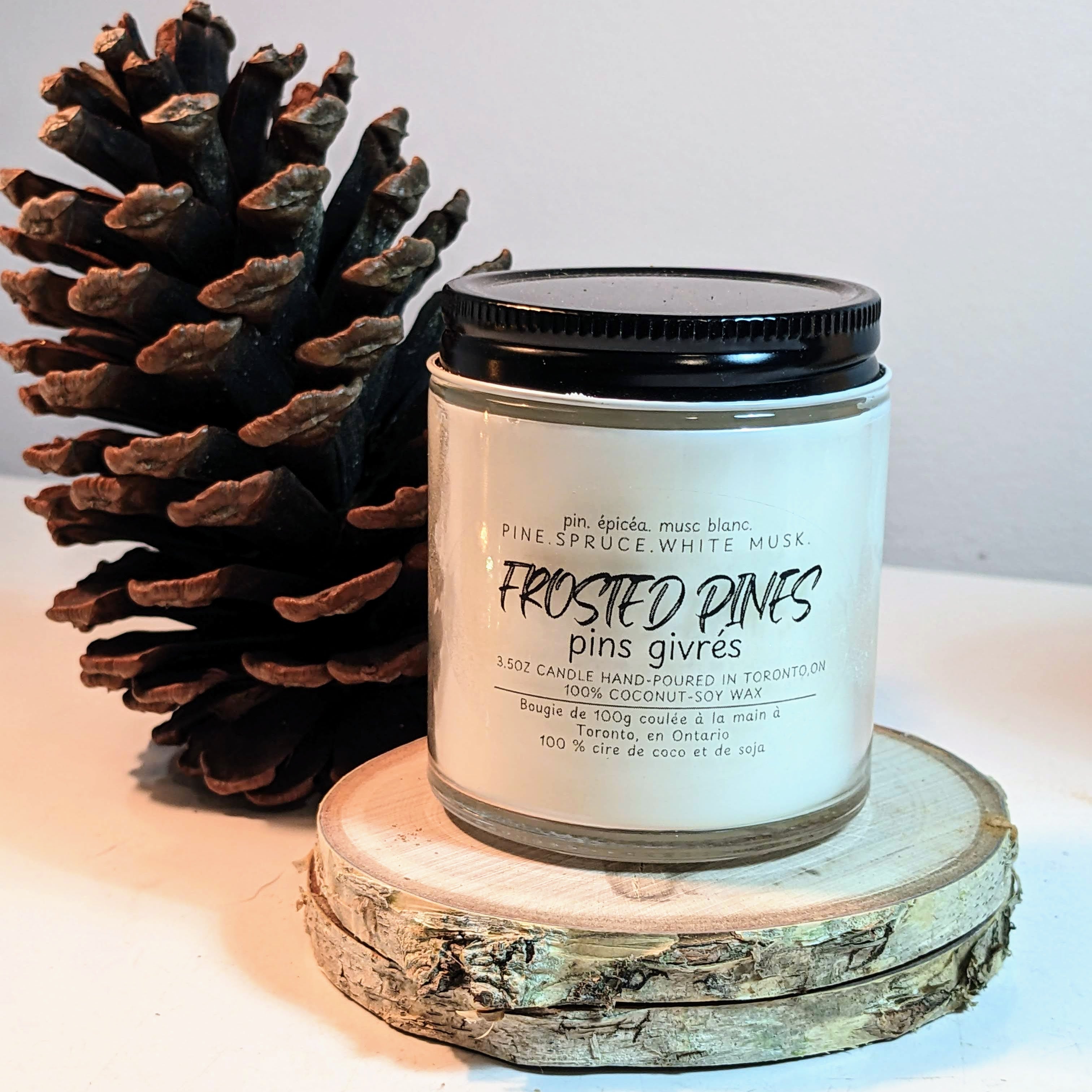 Candle labeled 'Frosted Pines' with a pine cone on a wooden surface