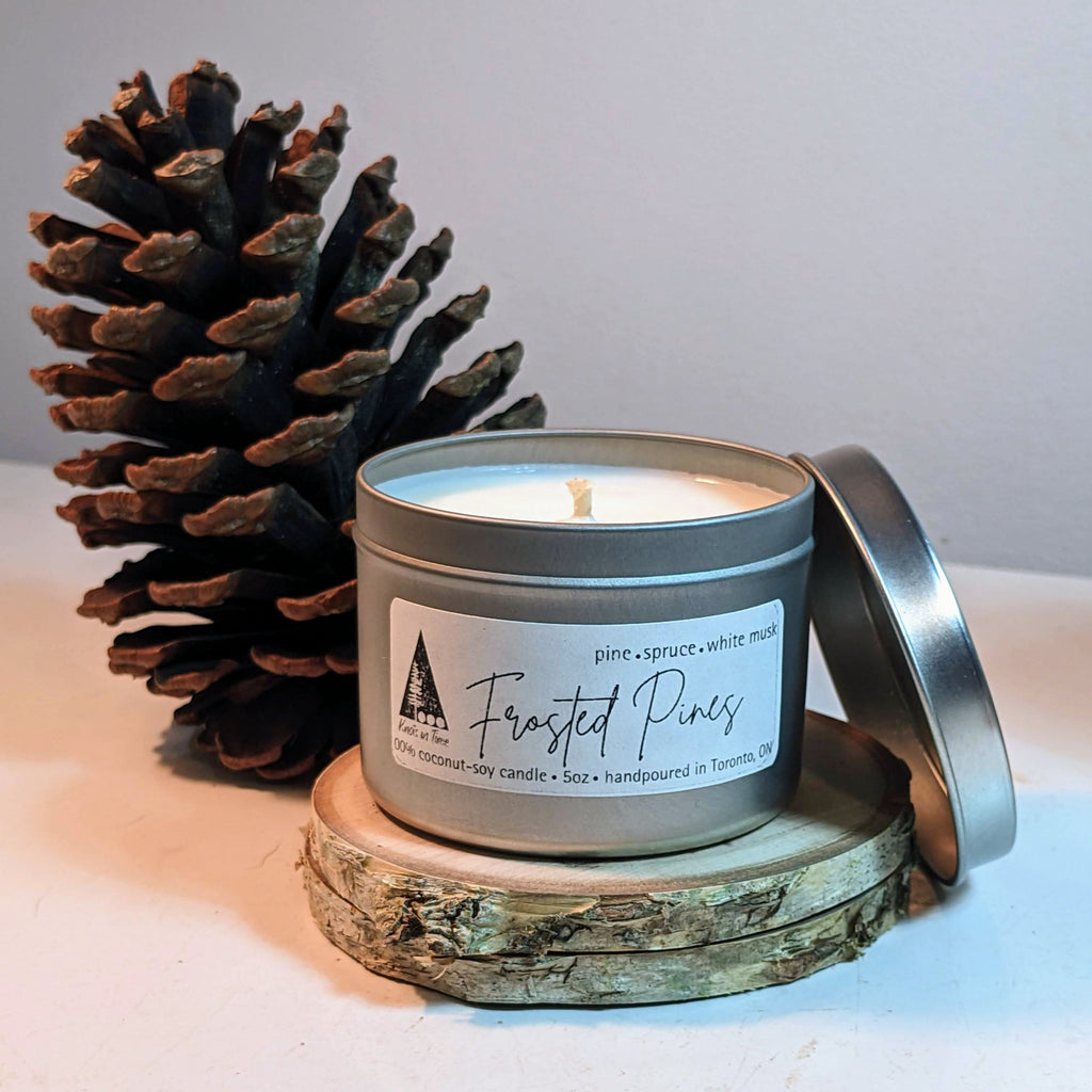 Frosted Pines candle in a tin with a pine cone on a wooden coaster.