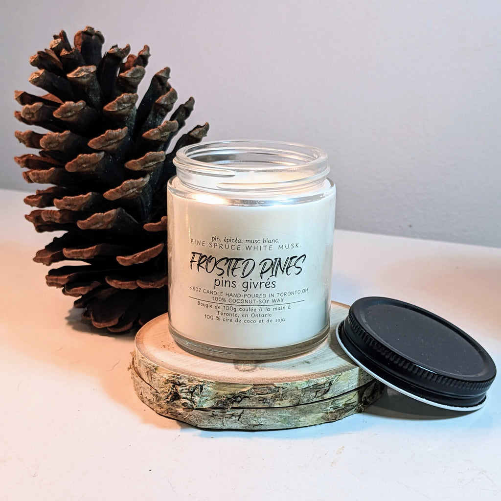 Candle jar labeled 'Frosted Pines' with a pine cone on a light surface