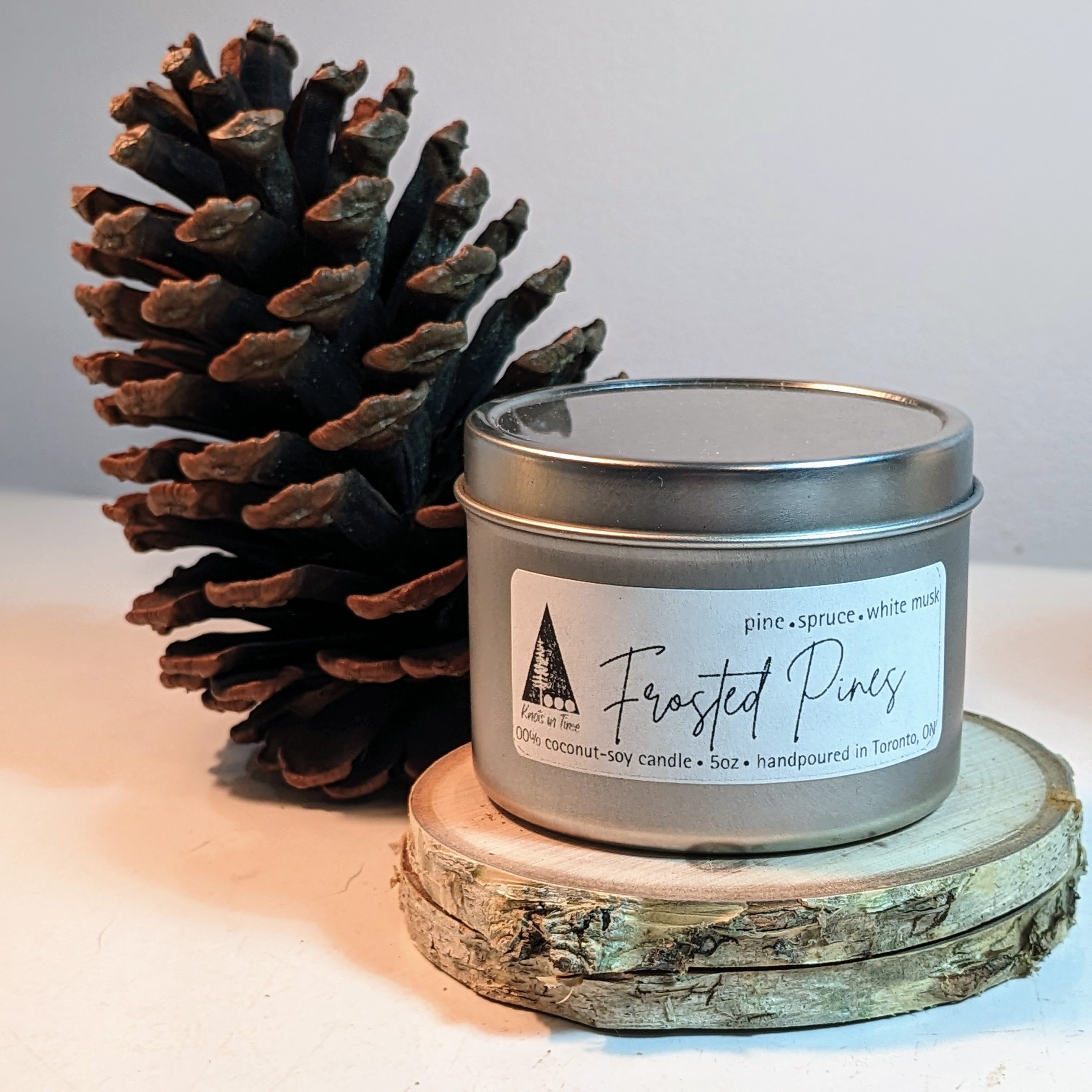 Candle labeled 'Frosted Pines' with a pine cone on a light background