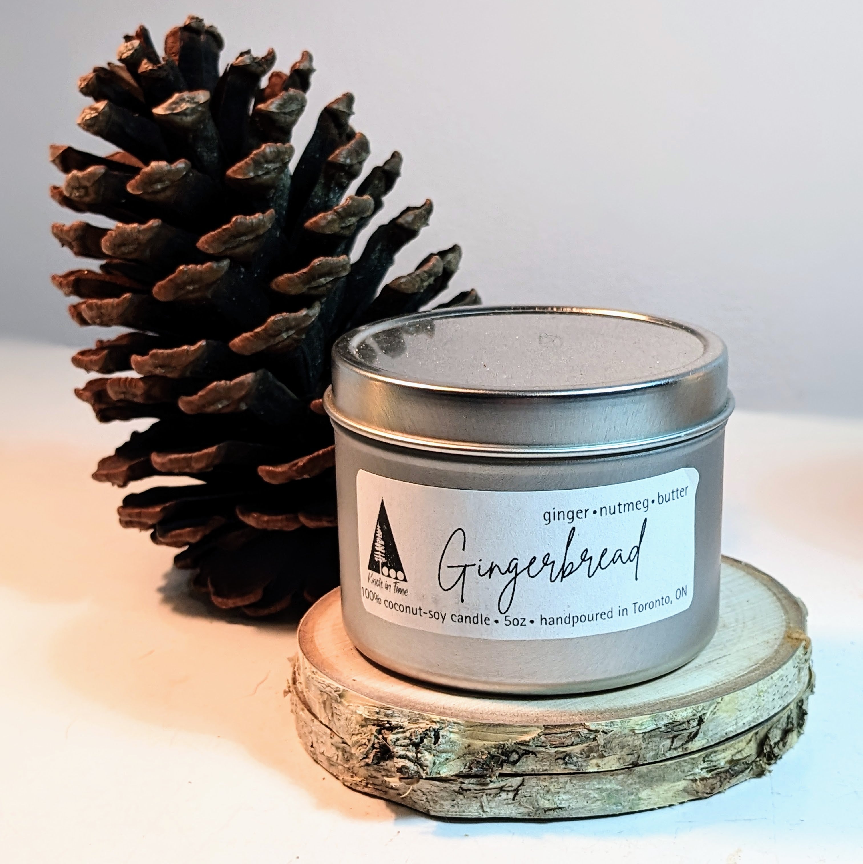 Gingerbread scented candle in a tin with a pine cone on a wooden block