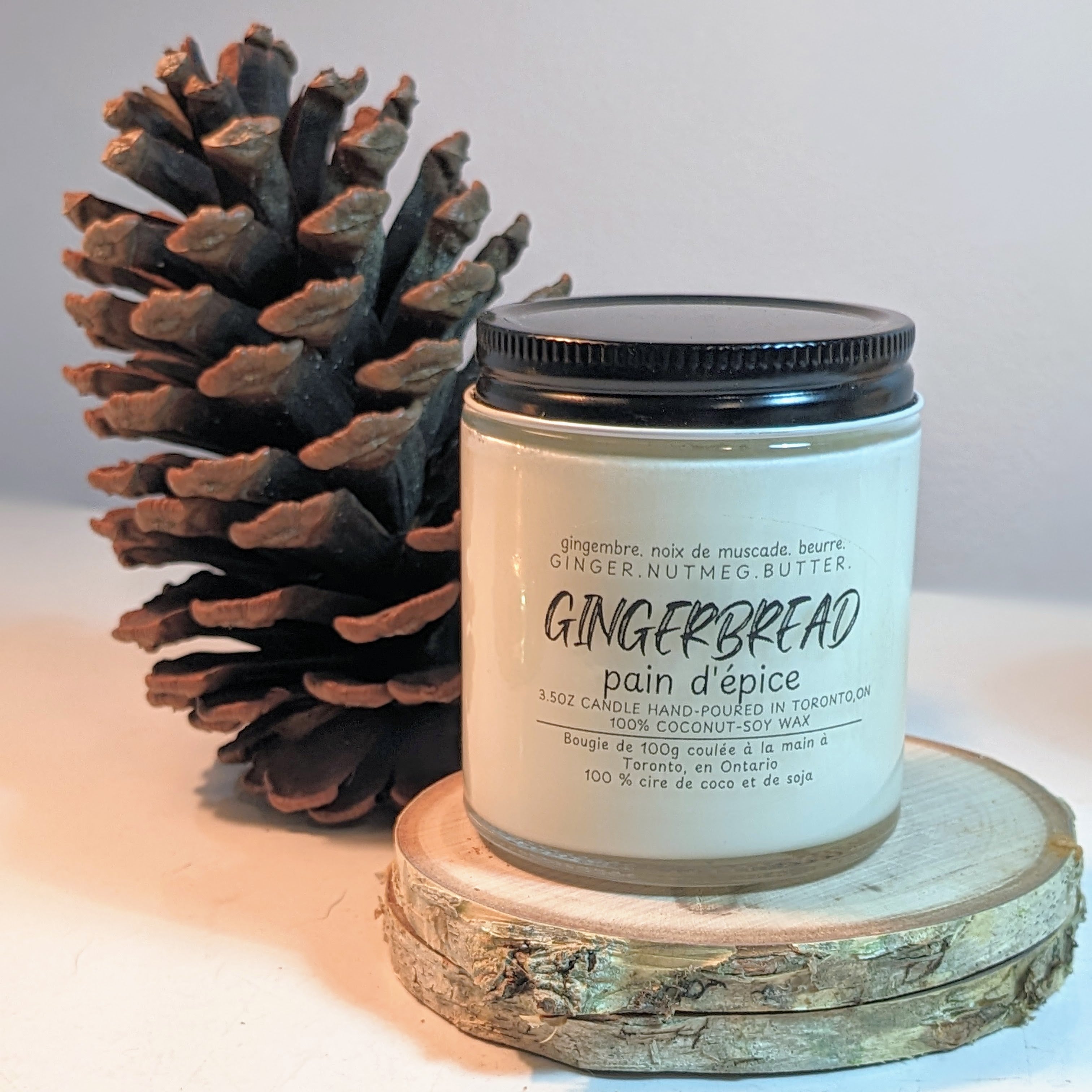 Gingerbread scented candle with a pine cone on a wooden surface