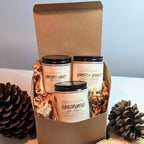 Three candles in a cardboard box with decorative items on a light surface.