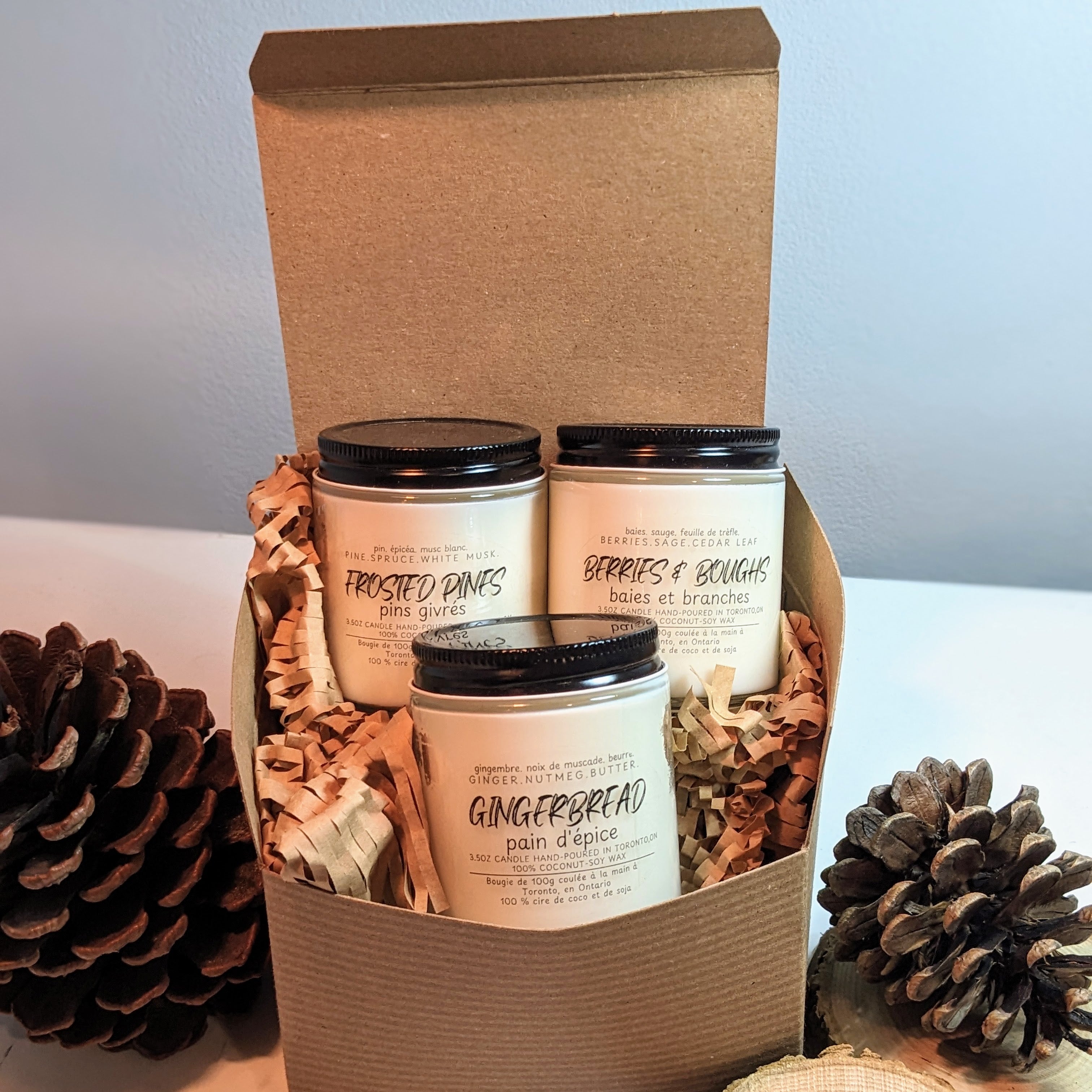 Three candles in a cardboard box with decorative items on a light surface.