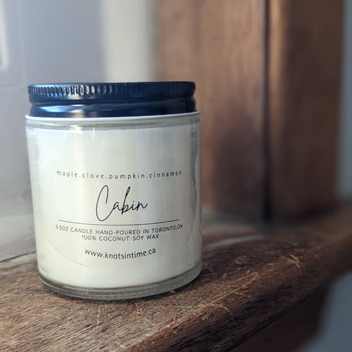 Candle labeled 'Cabin' with a black lid on a wooden surface