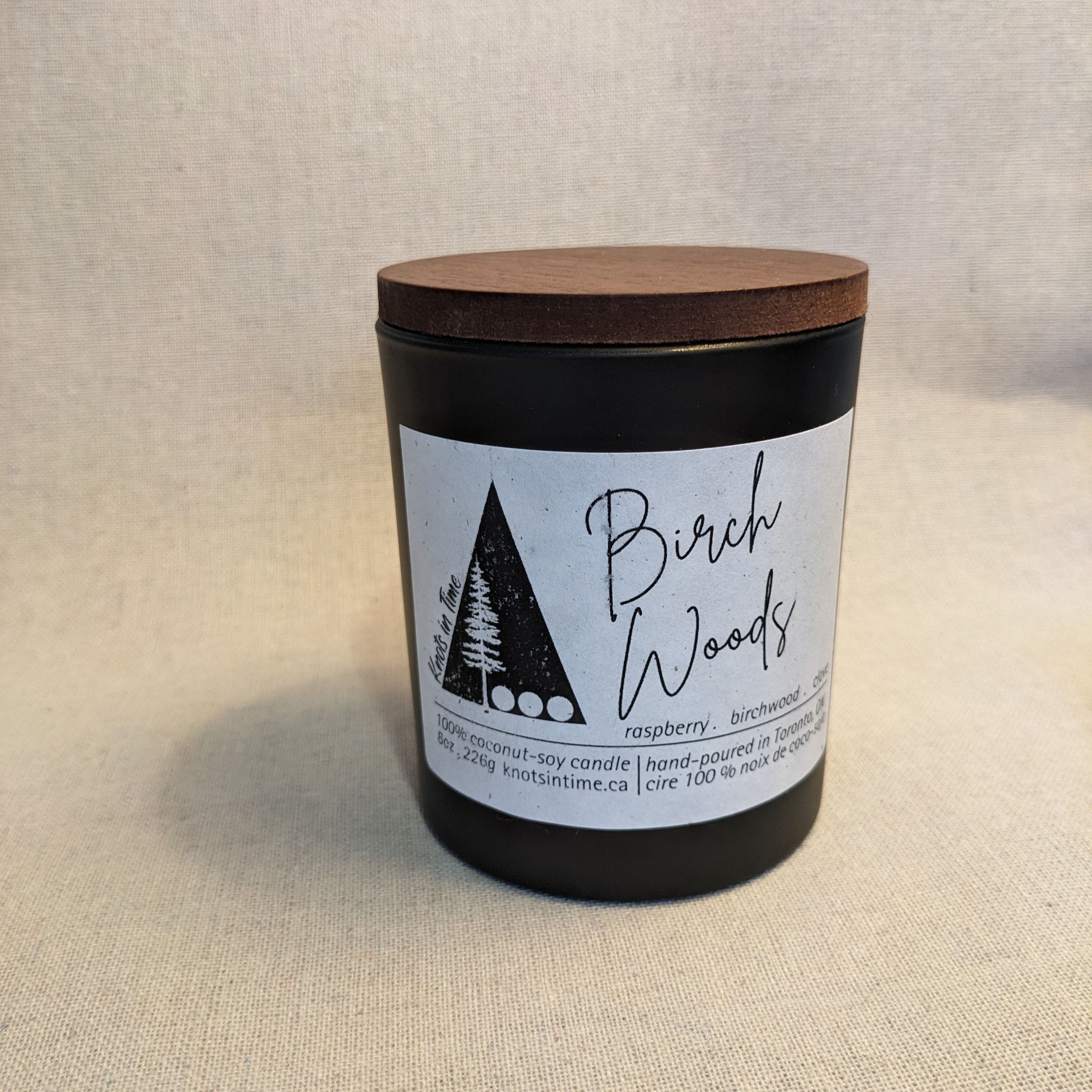 black glass candle with wood lid on a linen texture background