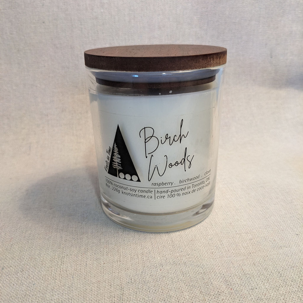 Candle jar labeled 'Birch Woods' with a wooden lid on a textured surface