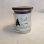 Candle jar labeled 'Birch Woods' with a wooden lid on a textured surface