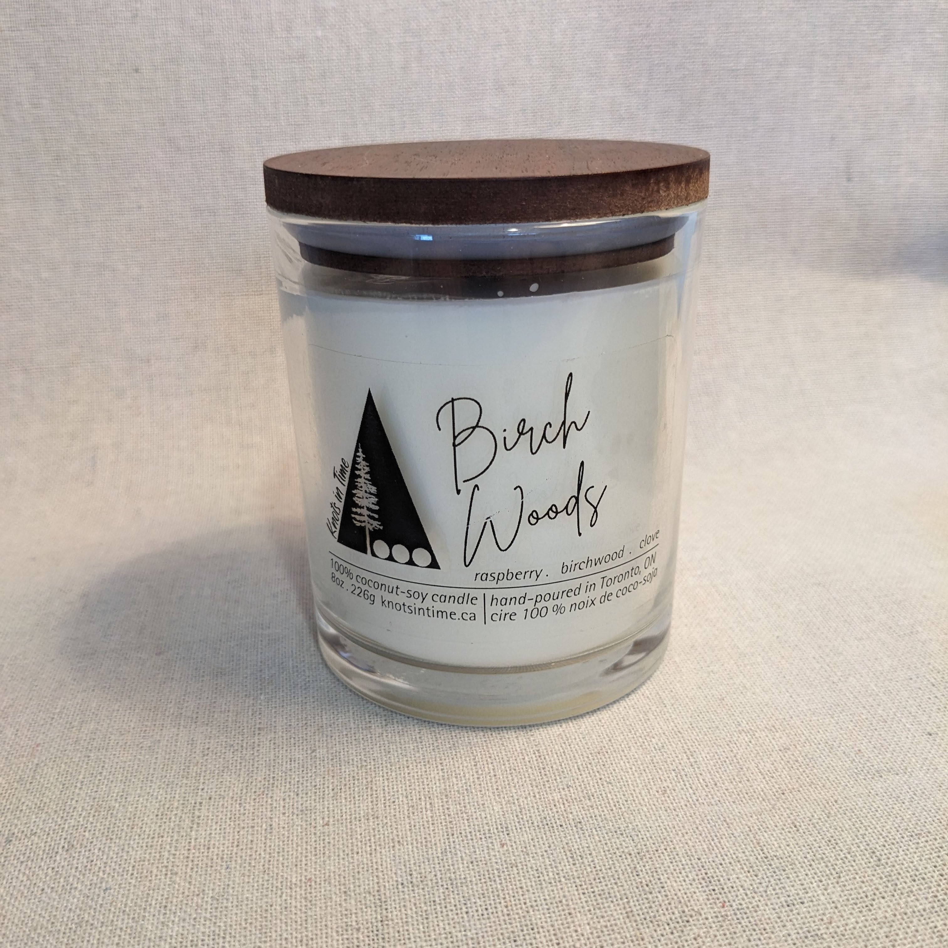 Candle jar labeled 'Birch Woods' with a wooden lid on a textured surface