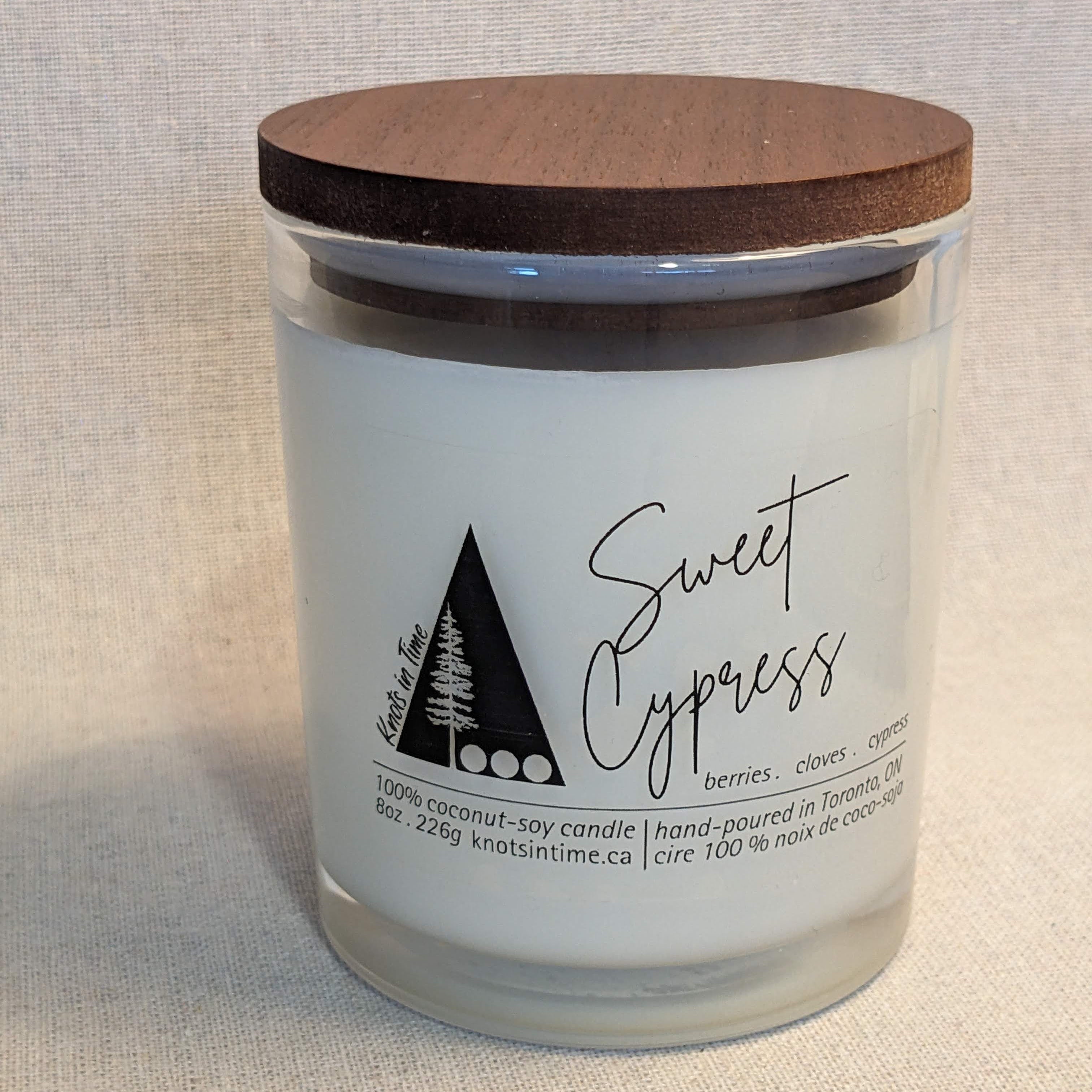 Candle with wooden lid labeled 'Sweet Cypress' on a neutral background