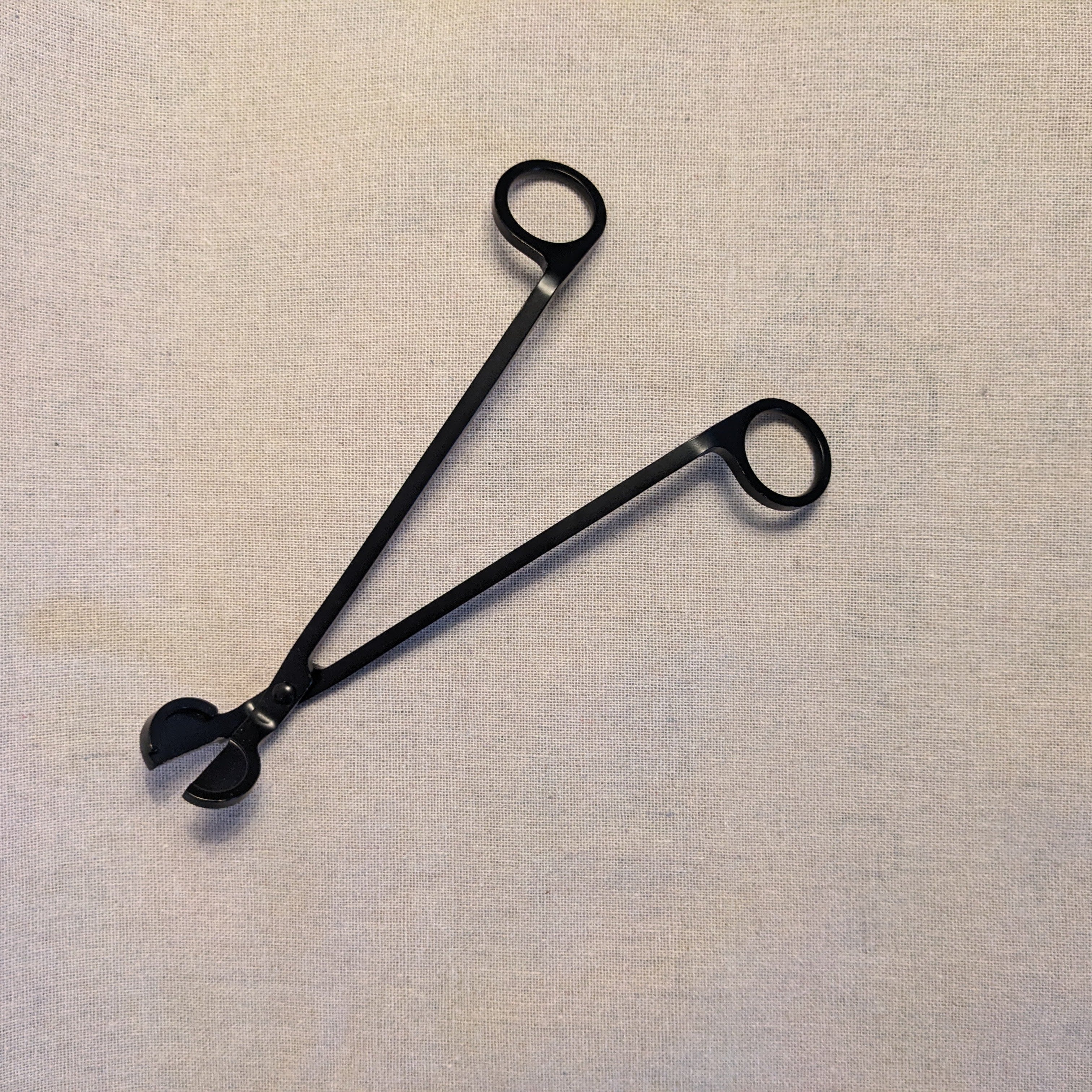 Black metal wick trimmer on a linen fabric background