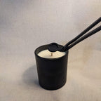 Black candle with a metal wick trimmer on a linen texture background