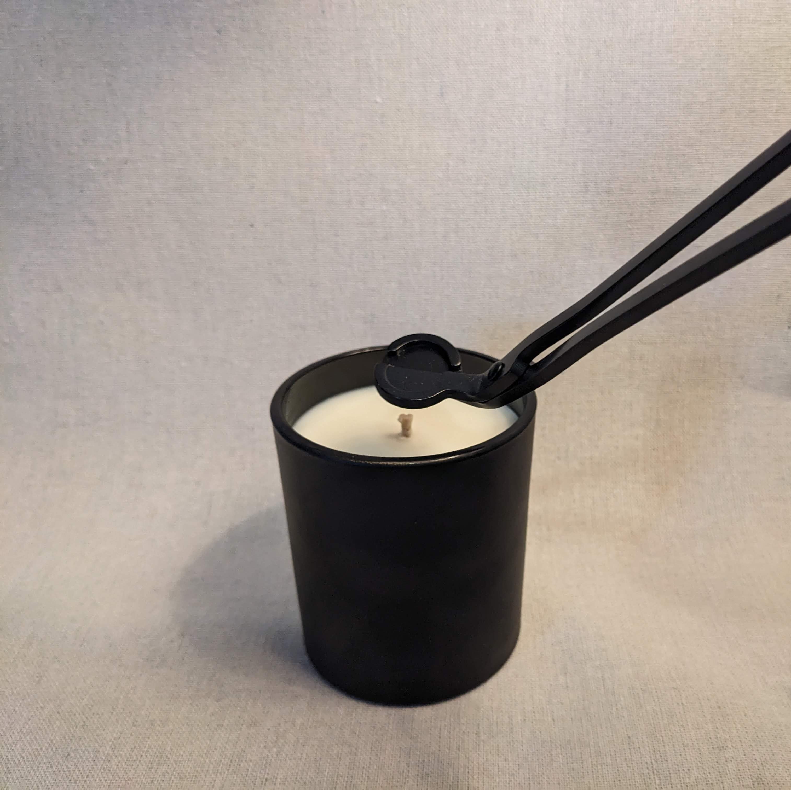 Black candle with a metal wick trimmer on a linen texture background
