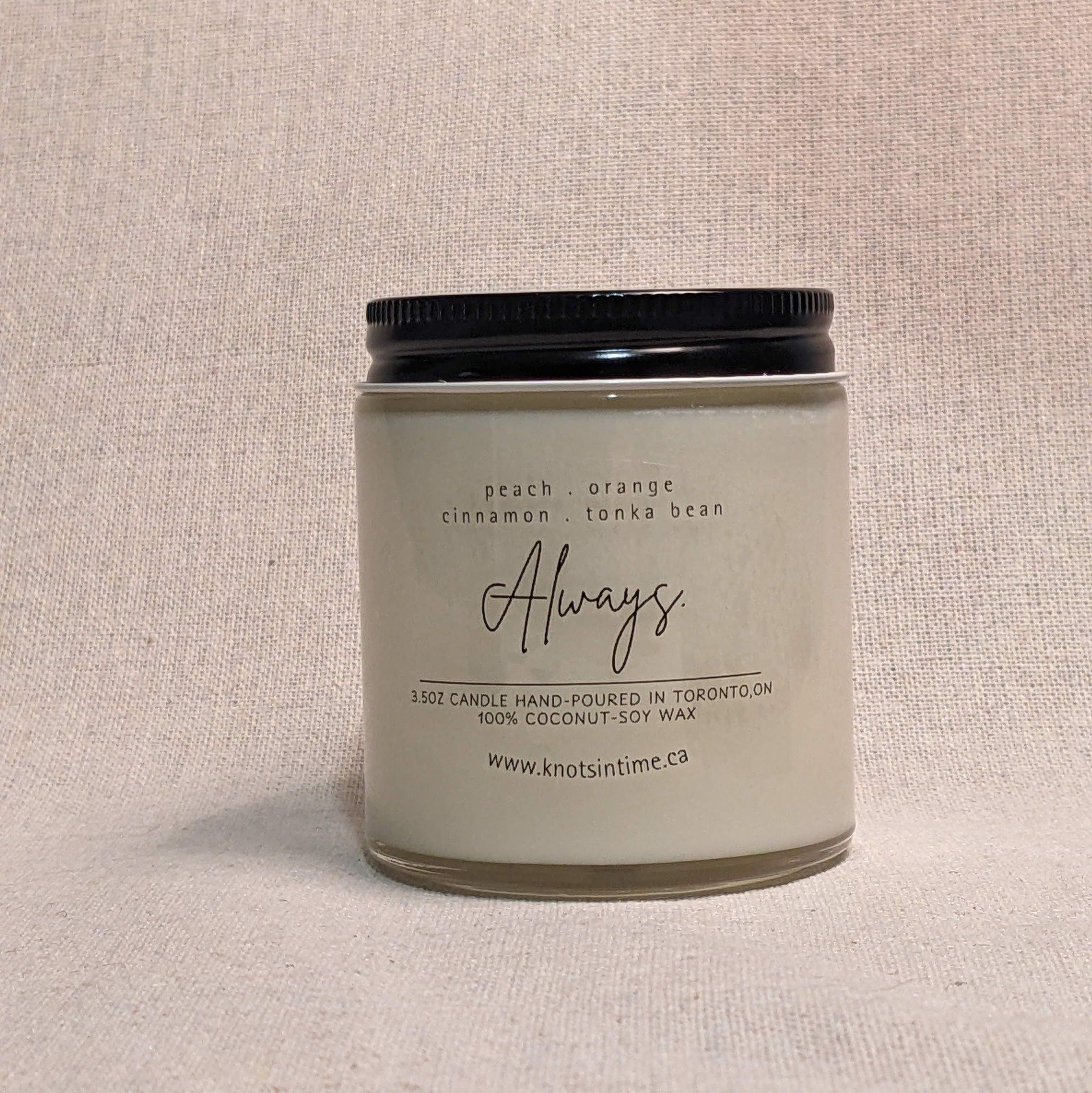 Clear candle jar with a black lid and clear label on a linen texture background