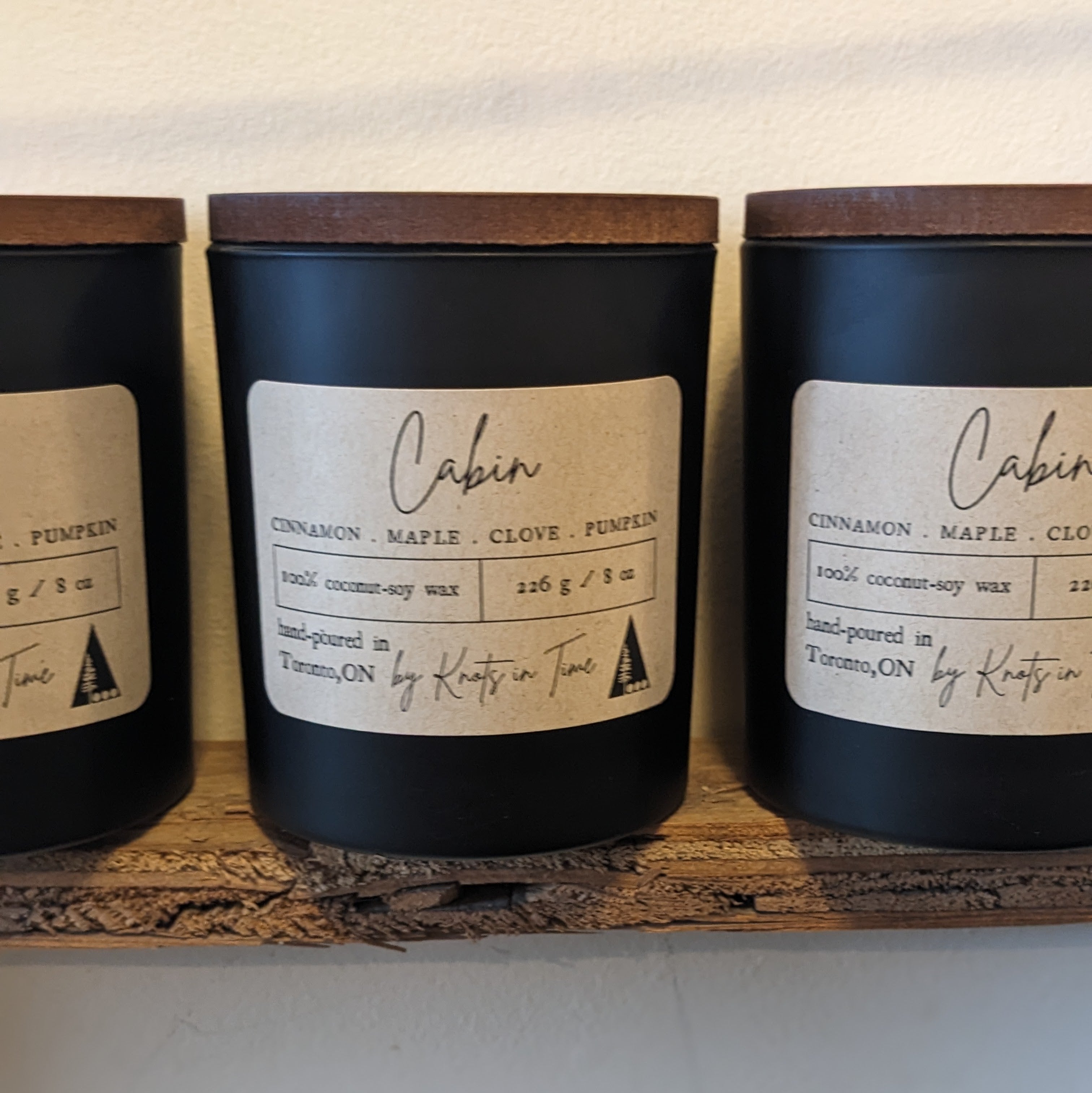 Three candles labeled 'Cabin' on a wooden shelf with a neutral background