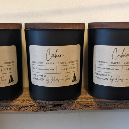 Three candles labeled 'Cabin' on a wooden shelf with a neutral background