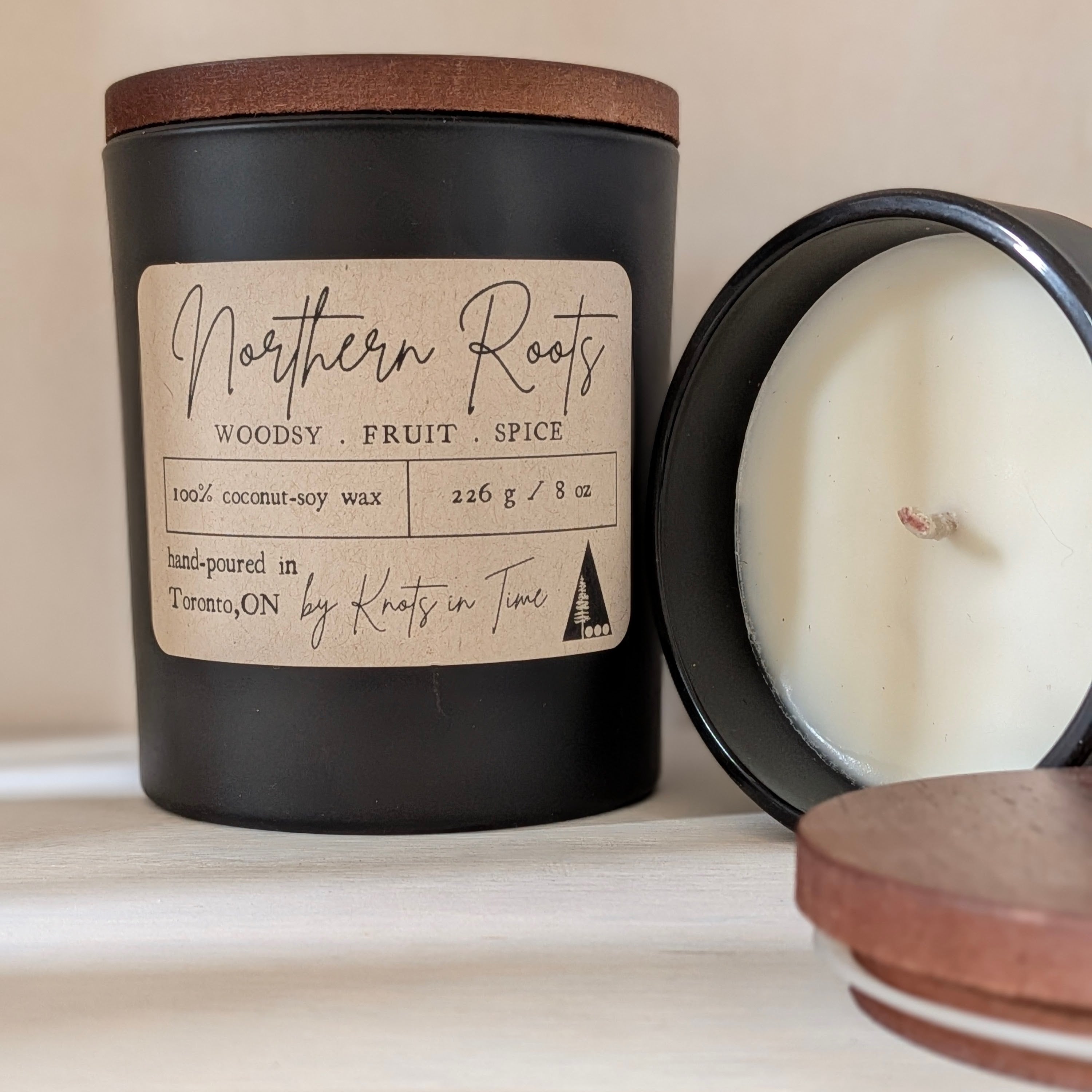 Black candle with wooden lid and 'Northern Roots' label on a neutral background