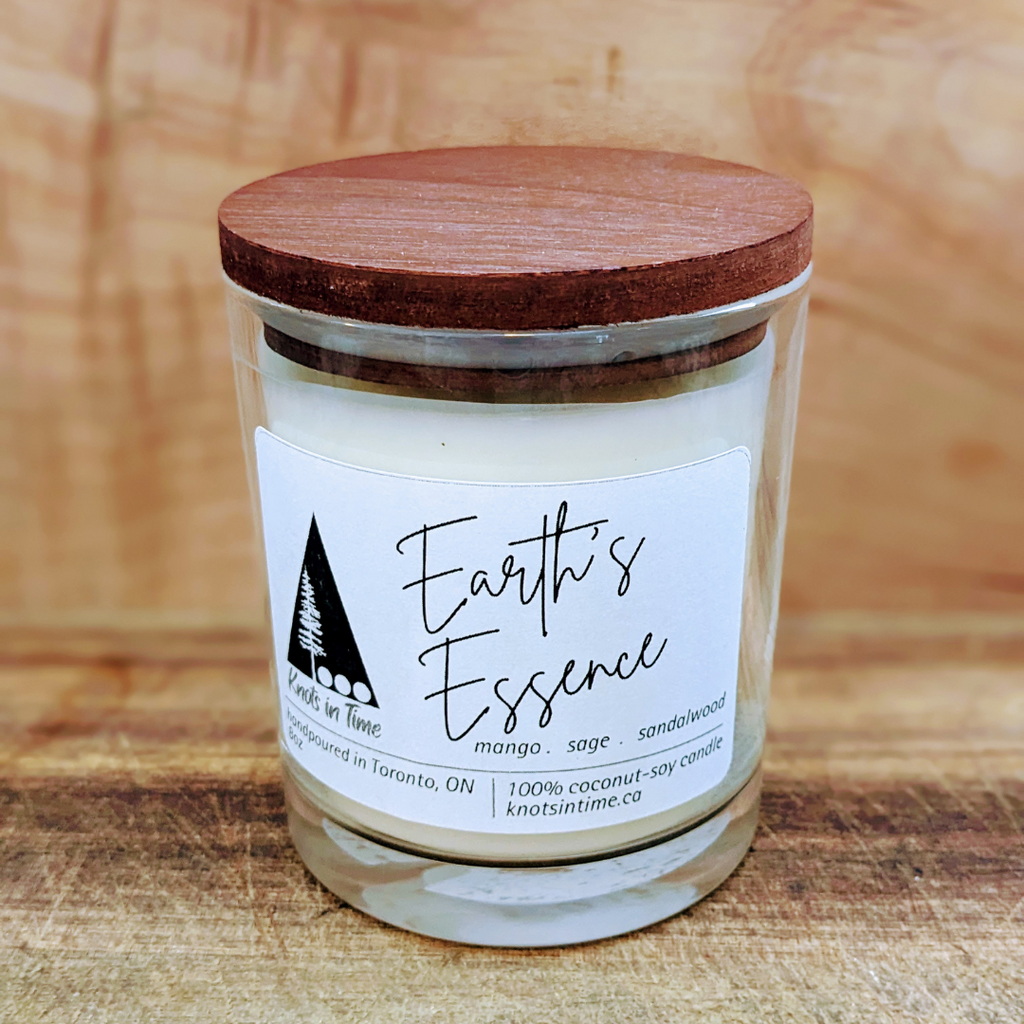 Candle jar with wooden lid and 'Earth's Essence' label on a wooden background