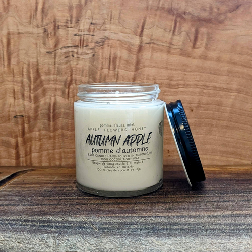 Candle labeled 'Autumn Apple' on a wooden surface