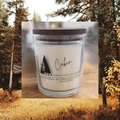Candle with 'Cabin' label in front of a forest background