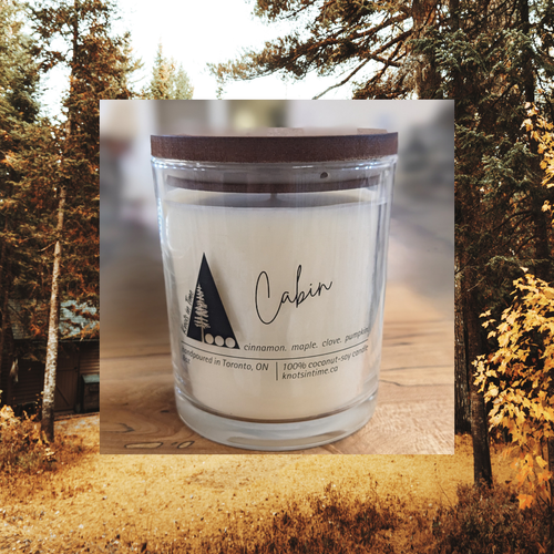 Candle with 'Cabin' label in front of a forest background