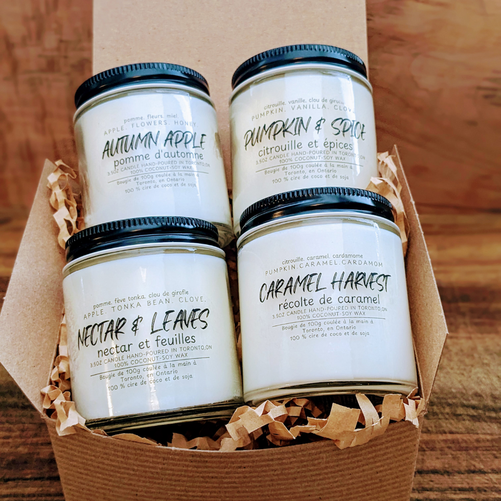Four candles with labels in a cardboard box on a wooden surface