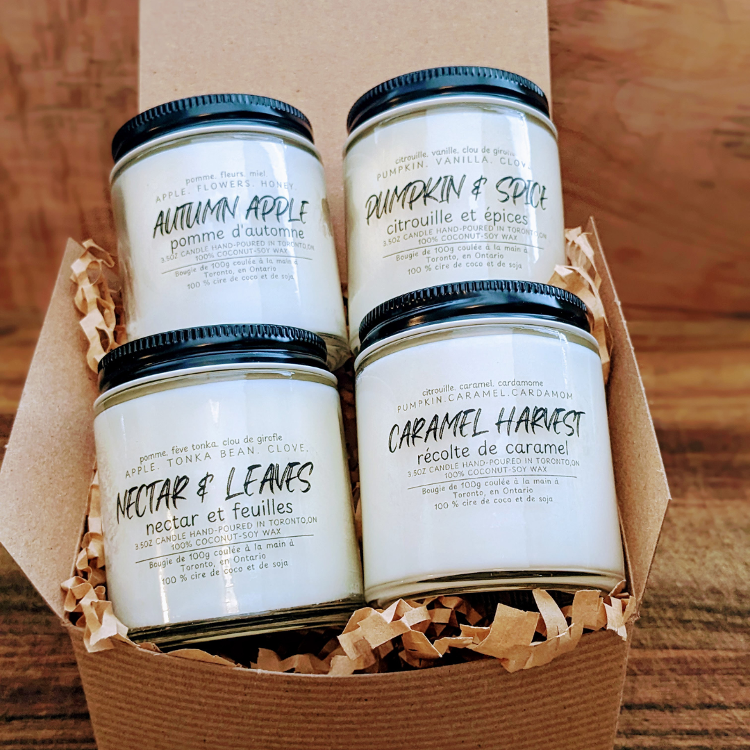 Four candles with labels in a cardboard box on a wooden surface