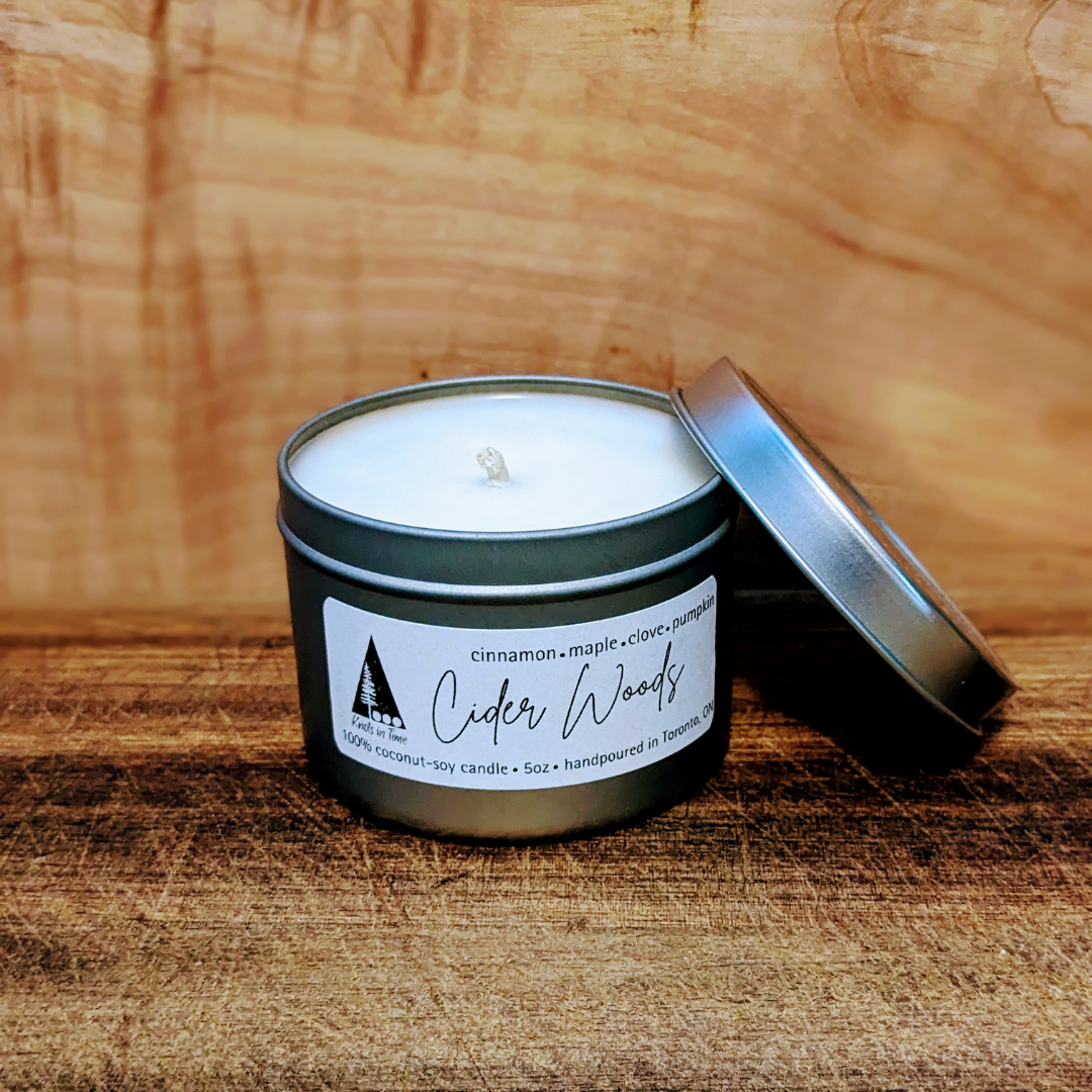 Candle in a tin labeled 'Cedar Woods' on a wooden surface